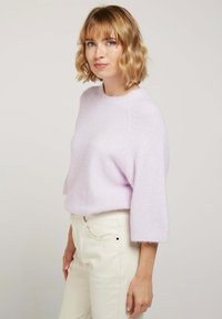Pull en lilas tricoté avec des manches courtes et larges et un col rond, associé à un pantalon couleur crème. Texture douce et coupe décontractée.
