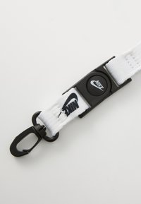 Cinghia in nylon bianco con accessori neri, fibbia circolare e logo Nike. Presenta un gancio per attacco e un motivo testurizzato sulla cinghia.