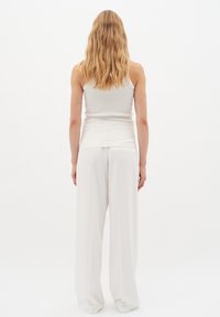 Valge soonikkoes tank top, millele on kombineeritud laiad, voolavad valged püksid. Kanga struktuur tundub sile ja kerge, luues lõdva silueti.