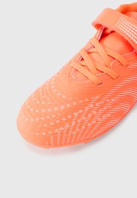 Φωτεινό πορτοκαλί αθλητικό παπούτσι με υφή από συνθετικό υλικό, διαθέτοντας λευκά σχέδια και λωρίδα βέλκρο πάνω από τα κορδόνια για ασφαλή εφαρμογή.