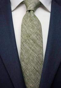 Vihreä teksturoitu solmio, jossa on viistokuvio, yhdistetty tummansiniseen pukuun ja valkoiseen kauluspaitaan.