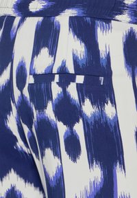 Marinblå och vit mönstrad tyg med abstrakta former; slät textur med en fickdetalj på högra sidan.