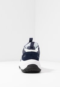 Marinblå och vit sportskor med övre del i mesh, mockadetaljer och en texturerad gummisula. Inkluderar en dragögla på hälen.