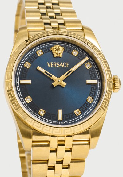 Χρυσό ρολόι Versace με μπλε καντράν, έμβλημα της Μέδουσας στη θέση 12, κρύσταλλους δείκτες ώρας και χρυστό μπρασελέ με συνδέσμους, δείχνει ώρα 10:09.