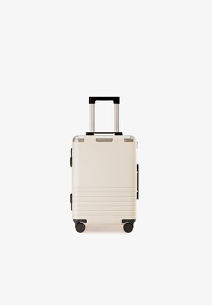 Harde koffer in crème met gegroefd textuur. Voorzien van een uitschuifbaar handvat, zwarte accenten en vier zwarte wielen voor mobiliteit.