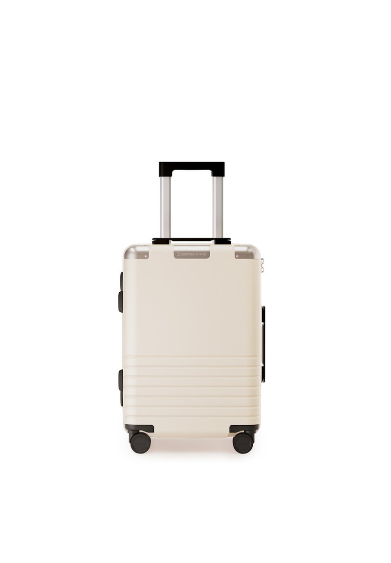 Hartschalenkoffer in Creme mit gerippter Textur. Verfügt über einen teleskopierbaren Griff, schwarze Akzente und vier schwarze Rollen für die Mobilität.