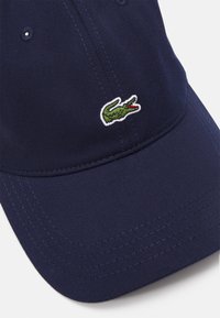 Marinekék baseball sapka bordázott textúrával, a bal elülső panelen zöld és piros hímzett krokodil logóval.