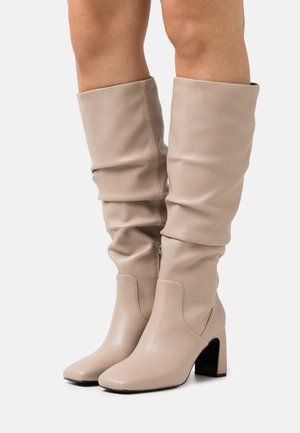 Beige knee-high boots in smooth leather with a slouchy design, square toe, and block heel, featuring a side zipper for closure.