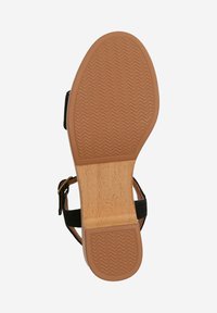 Black sandal with a textured brown rubber sole, featuring a wooden insole. The outsole shows a zigzag pattern for grip.