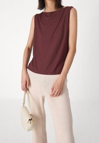 Burgundy ärmlös topp med avslappnad passform och ribbad textur, i kombination med ljusbeige ribbade byxor och en liten krämfärgad handväska.