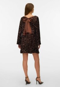 Ruda blizgučių suknelė su ilgomis rankovėmis, kaspinu ant nugaros ir platėjančiu sijonu. Dėvima su dirželiais aukštakulniais bateliais.