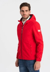 Giacca softshell rossa con cappuccio, zip frontale e tasche laterali. Dotata di polsini elasticizzati e texture liscia. Logo sulla manica.