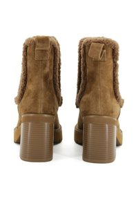 Stivaletti alla caviglia in suede marrone con fodera in pelliccia sintetica, tacchi spessi e scanalati, e una suola liscia e resistente. Presentano una linguetta per un facile indossamento.