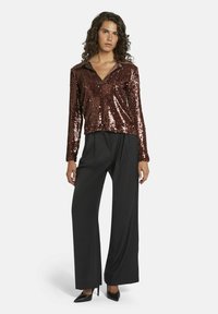 Bronzen pailletten top met lange mouwen en een kraag, gecombineerd met zwarte wijde broek en zwarte puntige hakken, die een glanzende, gestructureerde uitstraling bieden.
