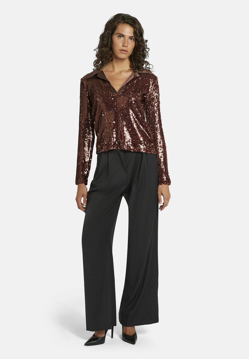 Haut long à manches en sequins bronze avec un col, associé à un pantalon noir à jambes larges et des talons aiguilles noirs, offrant une apparence brillante et texturée.