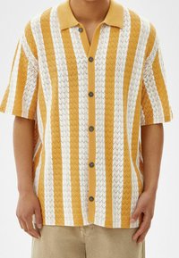 Geel en wit gestreept shirt met korte mouwen en een kraaghalslijn, textuurstof met een zigzagpatroon en vijf donkere knopen.