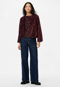 Top lungo a maniche con paillettes color borgogna, dal taglio rilassato, abbinato a jeans in denim scuro a gamba larga e scarpe con tacco nero.