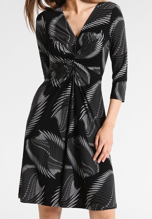 Robe noire longueur genou avec motifs tourbillonnants abstraits blancs, manches trois-quarts, et détail froncé torsadé à la taille.