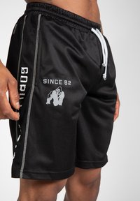 Zwarte mesh shorts met een elastische tailleband, witte trekkoord en zilveren accenten. Bevat een logo en de tekst "SINCE 82" aan de zijkant.