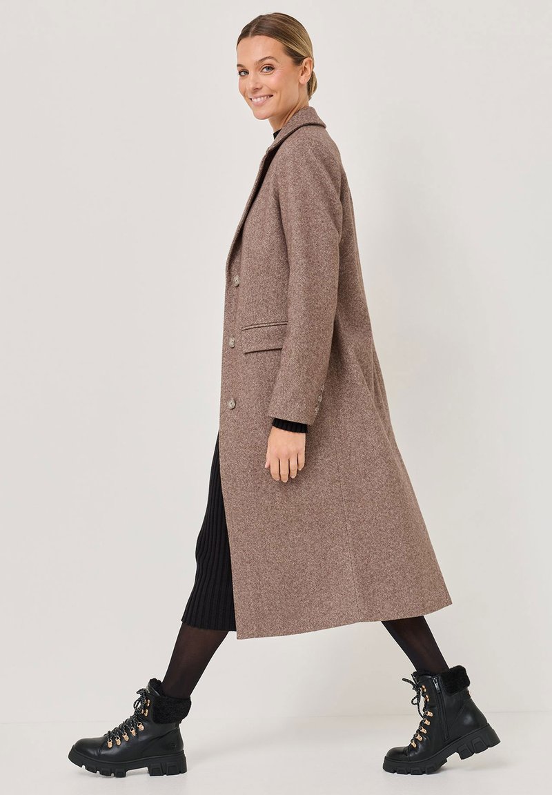 Brauner Woll-Mix-Mantel mit Reverskragen, seitlichen Taschen und zwei Knöpfen. Kombiniert mit schwarzen Schnürstiefeln mit Kunstfellbesatz.