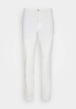 White linen pants with an elastic waistband and drawstring. Tapered design with elastic cuffs at the ankles. Soft texture, lightweight fabric.