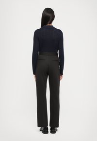 Námornícky klubový pletený sveter s dlhými rukávmi a vysokým golierom, skombinovaný s vysokými čiernymi nohavicami so rovnými nohavicami a čiernymi topánkami.