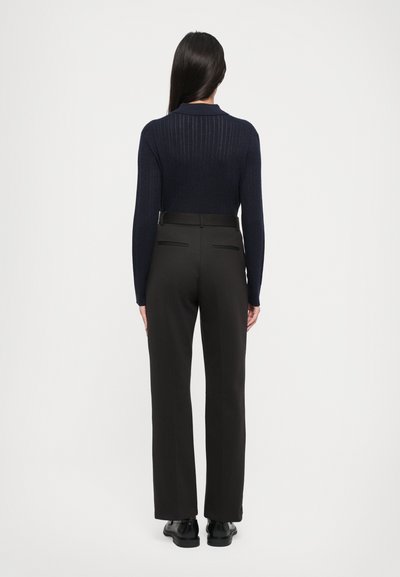 Tumes ribade lõngiliste varrukatega kõrge kaelusega kampsun, kombineerituna kõrge vöökohtadega sirgete mustade pükste ja mustade kingadega.