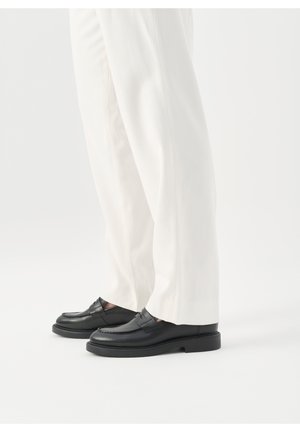 Sorte læderloafers med en hævet søm og glat, poleret tekstur, kombineret med hvide bukser, der viser et klassisk design.