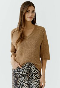 Brauner V-Ausschnitt Strickpullover mit kurzen Ärmeln, kombiniert mit einem Leopardenmuster-Rock. Strukturierter Stoff und lässige Passform mit seitlichen Schlitzen.