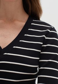 Svartvit randig stickad topp med V-ringning och ribbad struktur, som visar jämna horisontella ränder och en figurnära design.