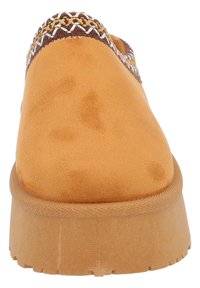 Gul mockaskinn slip-on sko med rund tå och texturerade bruna detaljer. Tjock sandfärgad sula med ett räfflat mönster längs kanten.