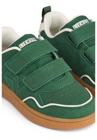 Green velcro sneakers made of soft material, featuring a gum sole, white accents, and stitched detailing. The design includes a side logo.