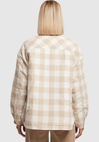 Chemise à carreaux beige à boutons, coupe décontractée, présentant de grands motifs à carreaux et un tissu doux et texturé. Comprend un col et des manches avec poignets.