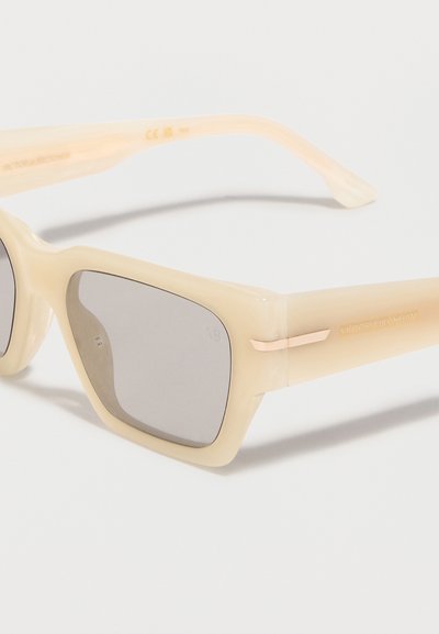 Μπεζ ορθογώνια γυαλιά ηλίου με ανοιχτό γκρι φακούς και χρυσές λεπτομέρειες στους βραχίονες, τοποθετημένα πάνω σε λευκό φόντο.