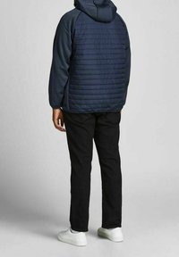 Marinblå pufferjacka med huva, med ett kviltat mönster. Bärs med svarta byxor och vita sneakers. Synlig strukturell detaljering på tyget.