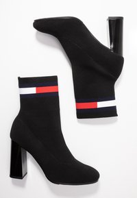 Černé kotníkové boty ve stylu sock s blokovým podpatkem. Lem je zdoben pruhy v červené, bílé a námořnické modré barvě. Vyrobeno z pružného materiálu pro pohodlí.