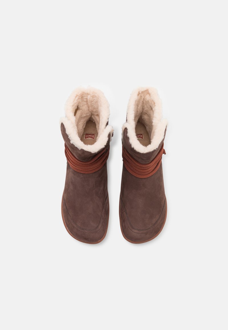Brune ankelstøvler i ruskind med en blød cremet pelsfor og brune snørebånd, der har en buet silhuet og teksturerede gummisåler.