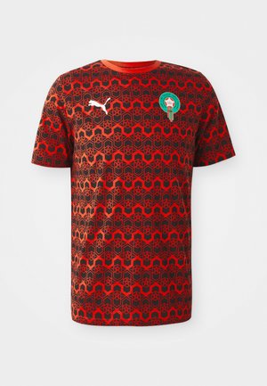 Punainen lyhythihainen T-paita, jossa on geometrinen musta kuvio, pyöreä kaula-aukko ja vihreä logo valkoisella logolla rinnassa.