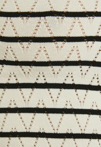 Stickad tyg med ett växlande mönster av krämfärgade och svarta ränder med triangulära utskärningar, vilket ger en strukturerad, lager-på-lager utseende.