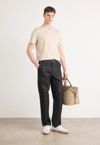 T-shirt beige à manches courtes, pantalon en denim foncé, baskets blanches et sac beige avec des accents marron. Design simple, coupe décontractée.