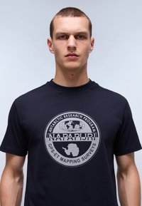 Námorně modré tričko s krátkými rukávy, na přední straně s velkým stříbrným grafickým designem globu a textem o antarktickém výzkumu.