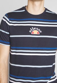 Camiseta a rayas azul marino con múltiples rayas horizontales en azul claro y blanco, que presenta un logo bordado en el pecho.