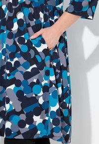 Värikäs mekko, jossa on sinisten, tummansinisten, harmaiden ja valkoisten pyöreiden muotojen kuvio; sisältää sivutaskut ja rento istuvuus.