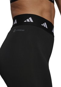 Svarta högmidjade leggings med elastisk midjeband och vit märkesdetaljering samt en slät, åtsittande textur. Labeln säger "AEROREADY."