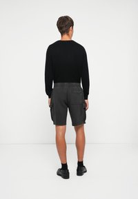 Sort ribbet sweater med lange ærmer, parret med grå cargo-shorts med sidelommer og elastisk talje, båret med sorte sko.