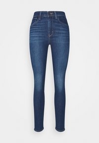 Jeans ajustados de denim azul oscuro con una textura suave, de cintura alta, y diseño clásico de cinco bolsillos. Detalles desgastados cerca de los muslos.