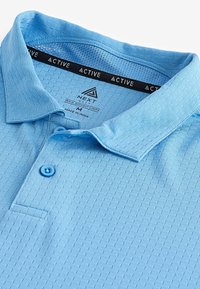 Himmelblaues Poloshirt mit strukturiertem Design, Drei-Knopf-Leiste und kontrastierenden Knöpfen. Das Markenlabel im Kragen zeigt "NEXT" und "ACTIVE".