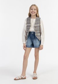 Biała bluzka o fakturze z bufkami, wzorzysta kamizelka z guzikami, dżinsowe szorty i białe sandały na paski. Prosty design, casualowy strój.