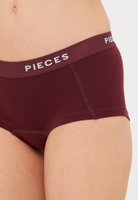 Burgundy színű pamut alsónadrág sima textúrával és fehér "PIECES" logóval az elasztikus derékpánton; lapos varrásokkal a kényelem érdekében.