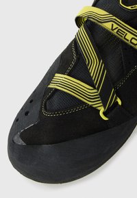 Scarpone da arrampicata nero con cinturini a strisce gialle che si incrociano sopra e una punta in gomma testurizzata.